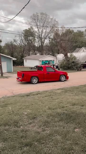 A lowered red mini truck driving down a neighborhood street